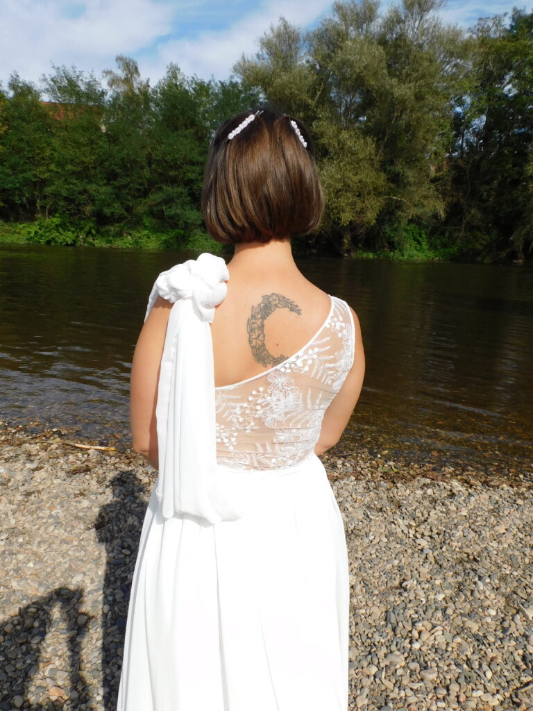 Les Précieuses- Robe de mariée Galène vue de dos. Haut asymétrique en dentelle et mousseline drapée sur l'épaule gauche. Une ceinture recouverte de dentelle met en valeur la taille de la mariée.