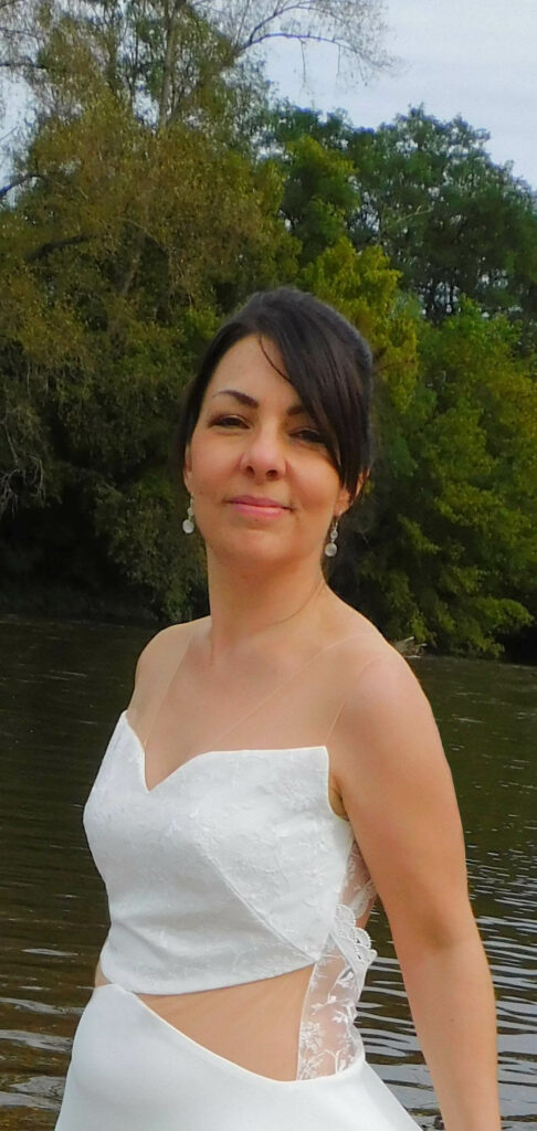 Les Précieuses - Robe de mariée Célestine vu de 3/4 face proche. Robe ajourée par le tulle effet peau nue à la taille et recouverte de dentelle très fine. Un galon de dentelle orne le dos nus.