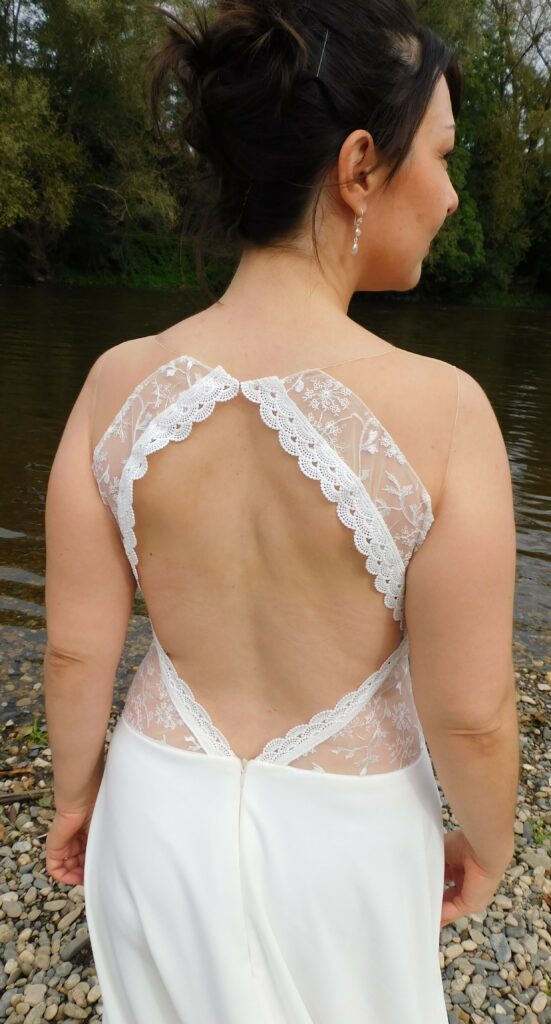 Les Précieuses - Robe de mariée Célestine vu de dos proche. Robe ajourée par le tulle effet peau nue à la taille et recouverte de dentelle très fine. Un galon de dentelle orne le dos nus.