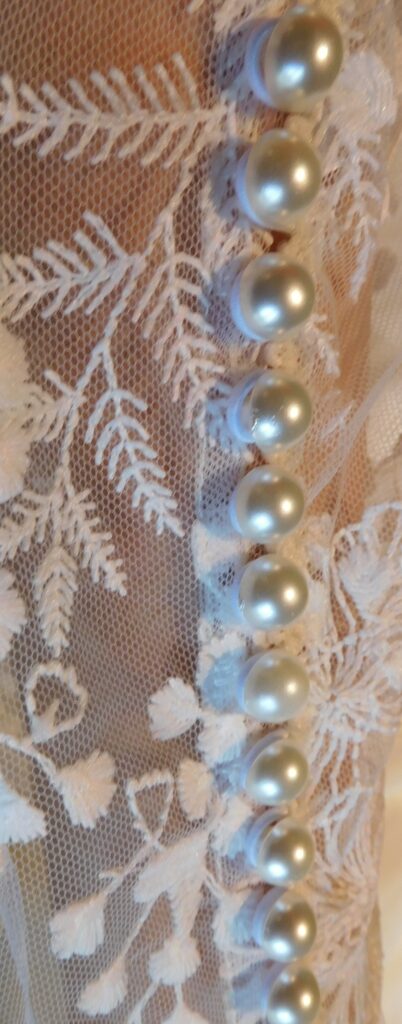 Les Précieuses - Robe de mariée Topaze détail. Avec ses manche longue en dentelle et son encolure bateau. Le dos est fermé par une myriade de petits boutons.