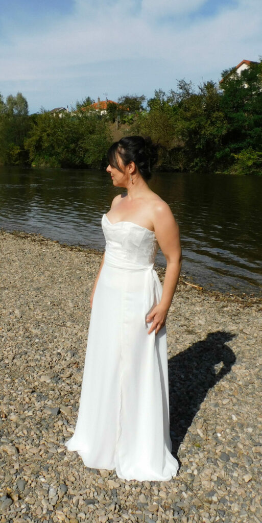Découvrez la robe de mariée Ambre. Une robe légère et fluide en crêpe. Dentelle en tulle brodé sur le bustier et drapé de mousseline. Vue de face/côté